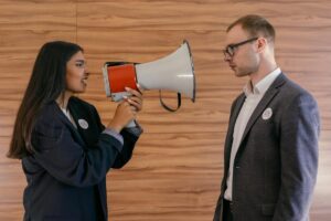 A woman using a megaphone to confront a man in a suit indoors, symbolizing political debate.